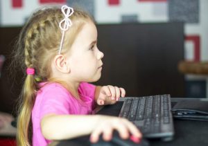 תמונת ילדה קטנה עם חולצה ורודה וצמות יושבת מול מחשב- מתוך פוסט בנושא שעות מסך זה לא כזה מלחיץ, באתר של מאור קפלן- מובילה תהליכי חינוך מיני במרחב הדתי