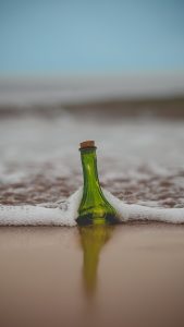תמונת בקבוק זכוכית ירוק שקוע בחוף הים והגלים מתנפצים עליו – מתוך פוסט הסתרה בזוגיות- מאור קפלן מובילה תהליכי חינוך מיני במרחב הדתי